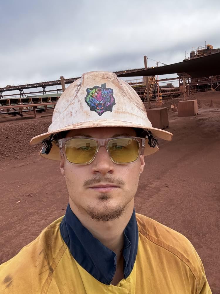 A worker in a hard hat in front of a mine site on red dirt
